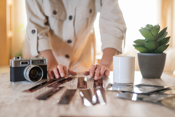Person's hands organizing strips of negative film and silver gelatin prints on a wooden table, with...