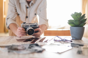 Hands holding a vintage rangefinder camera on a wooden table strewn with film strips, printed...