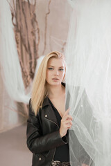 Portrait of a beautiful woman in a leather jacket near the curtain.