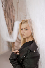 Portrait of a beautiful woman in a leather jacket near the curtain.