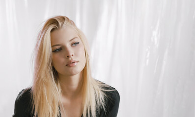Portrait of a very beautiful blonde in a black dress on an airy background.