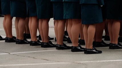 Uniformed women in teal skirts and polished black loafers stand aligned on marked pavement, showcasing disciplined formation during a formal outdoor gathering or drill.