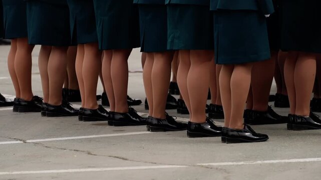 Uniformed women in teal skirts and polished black loafers stand aligned on marked pavement, showcasing disciplined formation during a formal outdoor gathering or drill.