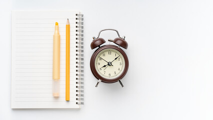 Vintage alarm clock with notebook, highlighter, and pencil, perfect for time management, study, or creative project concepts on a clean white surface