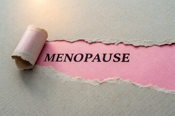 Close-up of a torn paper revealing the word 'MENOPAUSE' on a textured background with soft lighting