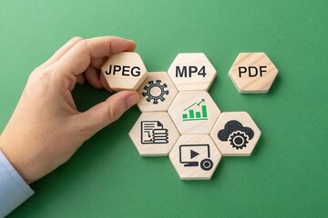 Hand arranging wooden hexagonal blocks with file formats and icons on a green background