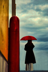 曇り空を眺める赤い傘の女性