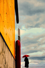 曇天を眺めながら雨を予感する赤い傘の女性