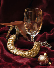 A still life for the New Year 2026, the Year of the Horse. An exquisite, elegant golden horseshoe and leather bridle are placed on a dark crimson velvet tablecloth next to a champagne glass and vintag