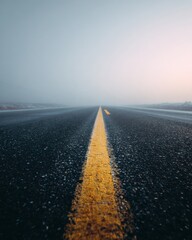 Serene and Foggy Road Through a Mysterious Landscape with a Single Yellow Line Leading Towards the Horizon