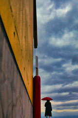 雲の流れを眺める赤い傘の女性