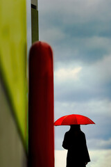 雲の流れを眺める赤い傘の女性