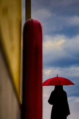 曇り空を眺める赤い傘の女性