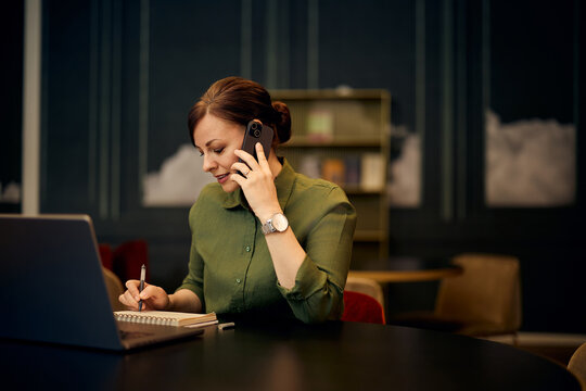 Professional Woman Working on Laptop While Speaking on Phone in Modern Office - Powered by Adobe