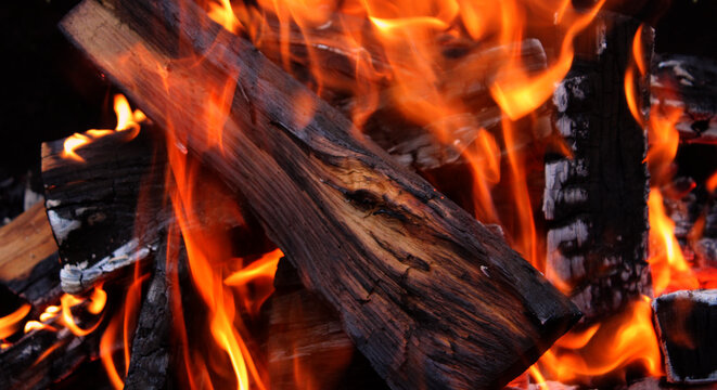 A large knotty log is engulfed in flames in an intensely burning fire in barbecue firebox detailed view
