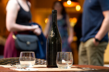Table with bottle and glasses at restaurant against defocused people