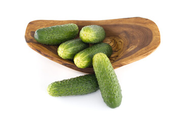 Group of fresh green cucumbers resting in a decorative wooden bowl against a white backdrop.