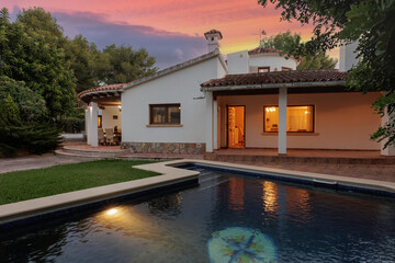 Evening view of a Mediterranean-style villa across an illuminated pool and green lawn.