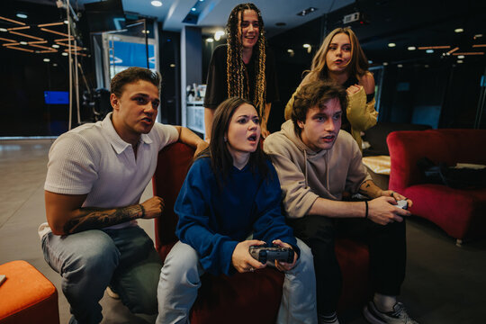 A close-knit group of friends deeply engaged in playing video games together, showcasing excitement and teamwork in a cozy modern setting. - Powered by Adobe