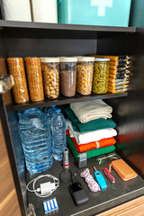 Stocked cupboard ready as part of alert, foresight and self sufficiency strategy. Organized emergency kitchen pantry with water bottles, packaged food, clothes, survival and communications supplies.