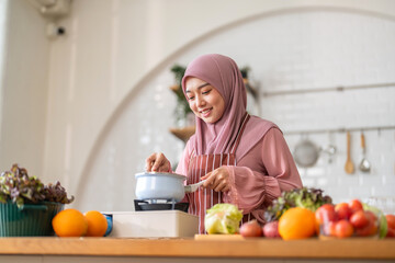 Muslim woman happy cooking healthy meal in kitchen wearing hijab making soup in pot with fresh vegetables food preparation activity nutrition, ramadan healthy recipe preparation, islamic food culture