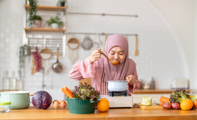 Muslim woman happy cooking healthy meal in kitchen wearing hijab making soup in pot with fresh vegetables food preparation activity nutrition, ramadan healthy recipe preparation, islamic food culture