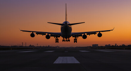 Fototapeta premium Airplane landing on runway at sunset with colorful sky backdrop 