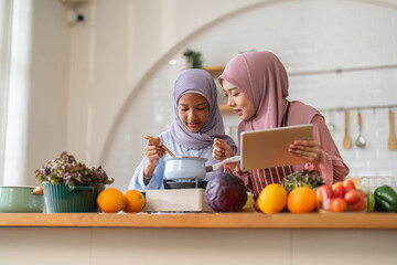 Muslim girl cooking with woman using tablet for recipe, halal food learning with technology, warm islamic family lifestyle, digital nutrition education for muslim kid, modern halal kitchen inspiration