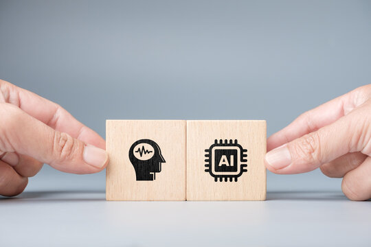 Close-up of two human hands holding wooden blocks with brain and AI chip icons symbolizing collaboration between human intelligence and artificial intelligence for innovation and creative application