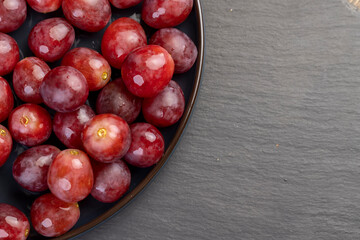 torn ripe grapes in drops of water on a blue plate , wet ripe and delicious red grapes on a plate on a black slate board