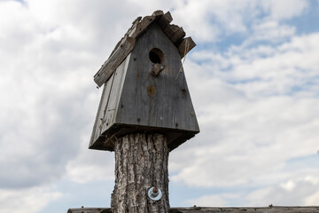 an old wooden birdhouse on a blue sky background, made of planks of an old birdhouse in cloudy weather