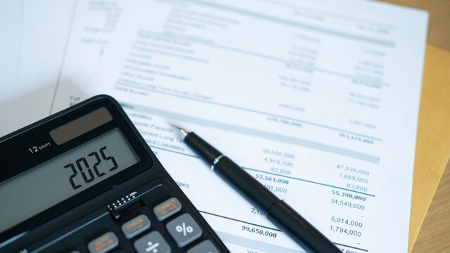 A black calculator showing 2025 placed on top of financial documents with a black pen nearby. The setup conveys focus on current financial reports and future investment direction.