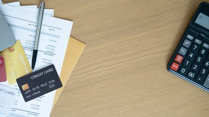 A black credit card with financial papers beside a silver pen on wooden desk with calculator partly...