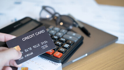 A hand holding a black credit card with calculator laptop eyeglasses and documents in background symbolizing payment management online shopping and secure financial planning.