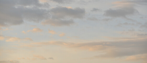 Multiple nuages dans un ciel rosé, bleu et gris au lever du soleil, format bannière