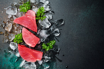Fresh raw tuna fillet on ice cut into steak on a stone background with seasonings and herbs