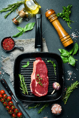 Juicy rib eye beef steak with spices and herbs on a pan. Ready to cook. On a dark stone background.