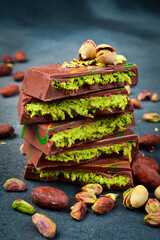 Dubai Chocolate bar with green kadayif and pistachio spread with pistachio nuts. Side view. On a dark stone background.