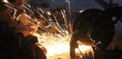 Worker Cutting Metal with Angle Grinder Producing Bright Sparks in street 
