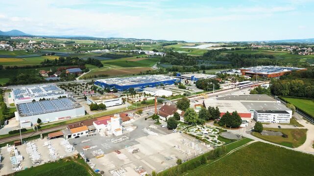 Aerial view of industrial buildings with solar panels and a train station amidst green fields, Aubonne, Vaud, Switzerland.