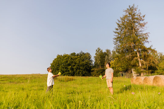 A father and son happily spend time together in a green field, playing catch under a clear blue sky on a bright sunny day. Their laughter fills the air as they bond over the activity - Powered by Adobe