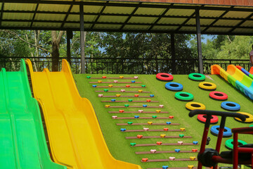 An elevated, wide view of a vibrant playground with a variety of multi-colored slides, a rock climbing wall, and tire rings. The scene is bright and highlights the many fun activities available.