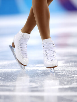 Sports photography - close-up of a figure skater's legs in figure skates on the ice of a stadium during the competition, blurred background, reportage style