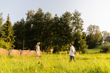 Bright sunlight shines as a father and son share joyful moments outdoors, playing catch in a lush green field surrounded by trees and hay bales