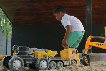 Little boy playing with children excavator in the sandbox.