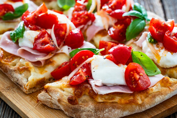 Pinsa Romana with boiled ham, cherry tomatoes, burrata cheese and basil leaves on wooden table	
