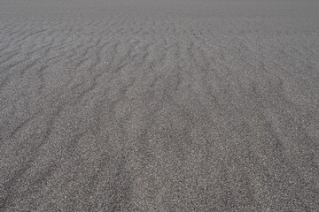 A beach with black volcanic sand, natural sand ripples and an ocean horizon