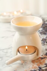 Aroma lamp with burning candle, sea salt and lavender flowers on white marble table, closeup