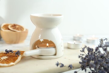 Aroma lamp with burning candle, lavender and dry orange slices on white table, closeup