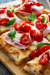 Pinsa Romana with boiled ham, cherry tomatoes, burrata cheese and basil leaves on wooden table	